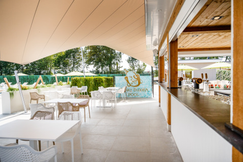Zona lounge exterior con mesas y sillas junto a Funky Buddha Pool en Resort Mooi Bemelen, Países Bajos.