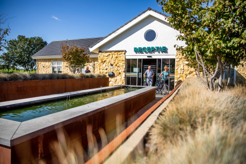 Two people with bicycles exit the reception of Resort Mooi Bemelen in the Netherlands on a sunny day.