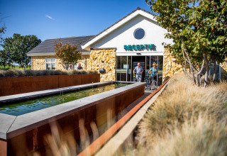 Dos personas con bicicletas salen de la recepción en Resort Mooi Bemelen en los Países Bajos durante un día soleado.