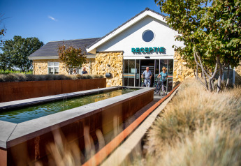Two people with bicycles exit the reception of Resort Mooi Bemelen in the Netherlands on a sunny day.