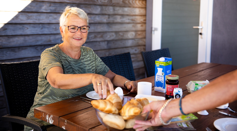 Mujer mayor desayunando al aire libre en Biebosch - tuinhuis, Resort Mooi Bemelen, Países Bajos.