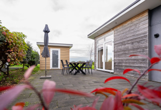 Terraza exterior con mesa, sillas y sombrilla junto a una cabaña de madera en Resort Mooi Bemelen, Países Bajos.
