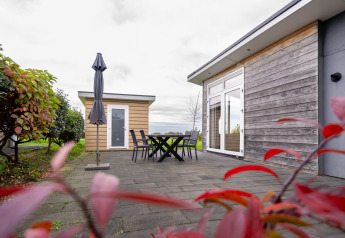 Udendørs terrasse med borde, stole og parasol foran en træbeklædt lodge på Resort Mooi Bemelen i Holland.