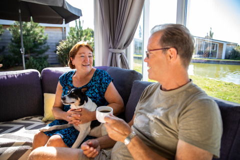 To glade mennesker sidder i en dagligstue ved Resort Mooi Bemelen i Nederlandene med en hund på skødet.
