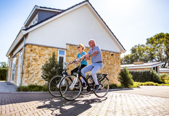 Zwei Personen fahren Fahrrad vor Biebosch - tuinhuis im Resort Mooi Bemelen in den Niederlanden an einem sonnigen Tag.