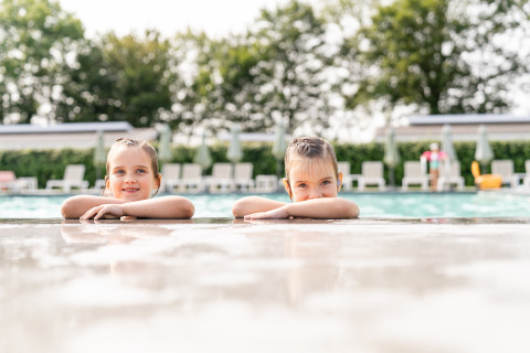 Dos niños descansan al borde de una piscina en Biebosch - tuinhuis, Resort Mooi Bemelen, Países Bajos, verano.