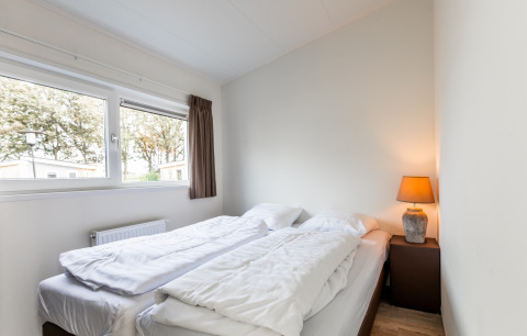 Helles Schlafzimmer im Biebosch - tuinhuis im Resort Mooi Bemelen, Niederlande, mit zwei Betten und Lampe.