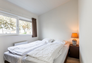 Helles Schlafzimmer im Biebosch - tuinhuis im Resort Mooi Bemelen, Niederlande, mit zwei Betten und Lampe.