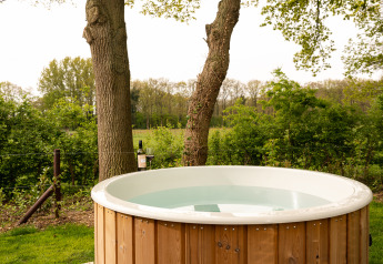 Vasca idromassaggio all'aperto circondata da alberi e natura in una sistemazione glamping, ideale per rilassarsi.