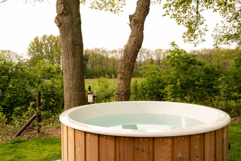 Buitenspa omgeven door bomen en groen bij een glampingaccommodatie, perfect om buiten te ontspannen.