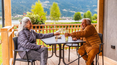 Pareja mayor disfrutando vino en la terraza de Enzian Waterfront, Ossiacher See, Austria, con vistas al lago.
