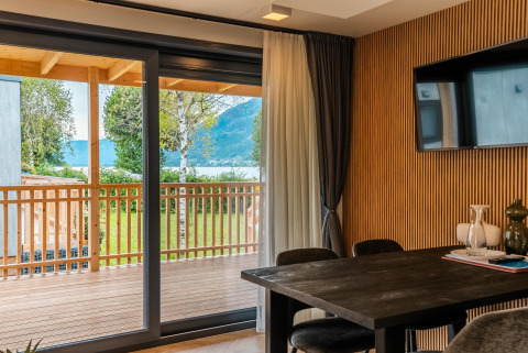 Moderne lodge met houten muur, grote tafel en schuifdeur naar terras aan Ossiacher See in Oostenrijk.