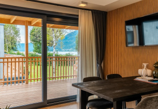Moderne lodge met houten muur, grote tafel en schuifdeur naar terras aan Ossiacher See in Oostenrijk.