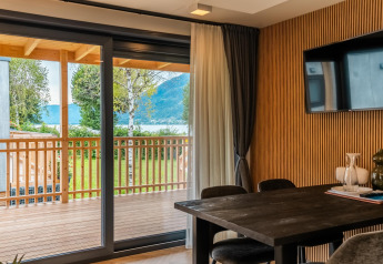 Interno di lodge moderno con tavolo in legno e porta finestra sulla terrazza, vista lago Ossiacher See, Austria.