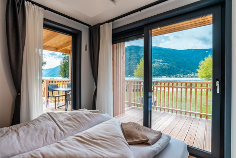 Lichte slaapkamer bij Enzian Waterfront, Ossiacher See, Oostenrijk, met zicht op meer, bergen en balkon.