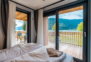 Lichte slaapkamer bij Enzian Waterfront, Ossiacher See, Oostenrijk, met zicht op meer, bergen en balkon.