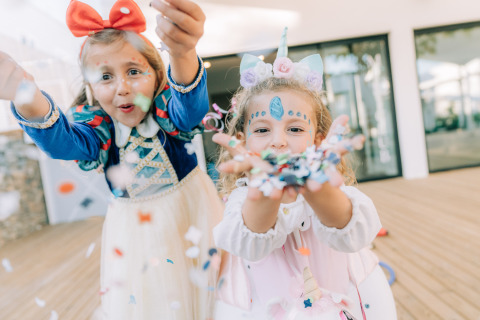 Dos niñas con disfraces coloridos lanzan confeti en Camping Costa del Sol Glamping Village, Andalucía, España.