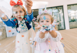 Twee kinderen in kleurrijke kostuums gooien confetti op Camping Costa del Sol Glamping Village, Andalusië.