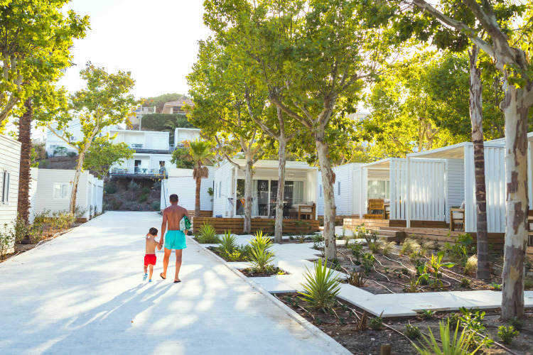 Vater und Sohn spazieren durch moderne Hütten mit Bäumen im Costa del Sol Glamping Village in Andalusien.