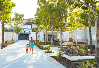 Far og søn går blandt moderne hytter omgivet af træer på Camping Costa del Sol Glamping Village i Andalusien.