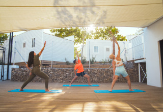 Tre persone praticano yoga su tappetini sotto una tettoia a Camping Costa del Sol Glamping Village, Andalusia.