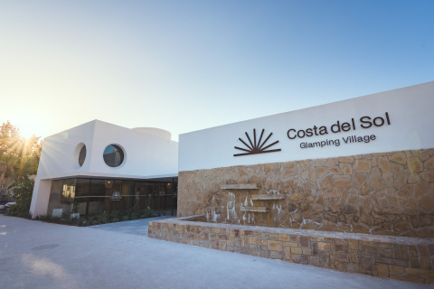 Entrada de Camping Costa del Sol Glamping Village en Andalucía, España, con edificio moderno y muro de piedra.