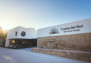 Entrance of Camping Costa del Sol Glamping Village in Andalusia, Spain, featuring a modern building and stone wall.