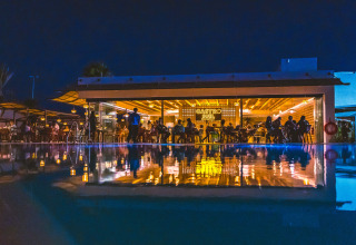 Night view of a poolside restaurant at Camping Costa del Sol Glamping Village, Andalusia, Spain, with reflections.