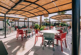 Zona de comedor exterior en Camping Costa del Sol Glamping Village con sillas coloridas y pérgolas de sombra.