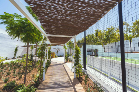 Pasarela de madera y pérgola junto a pista deportiva en Camping Costa del Sol Glamping Village, Andalucía, España.