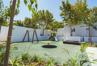 Legeplads med gynger, rutsjebane og karussel omgivet af træer på Camping Costa del Sol Glamping Village.