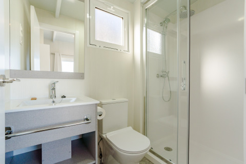 Moderne en lichte lodgebadkamer met douche, toilet, wastafel en een grote spiegel.