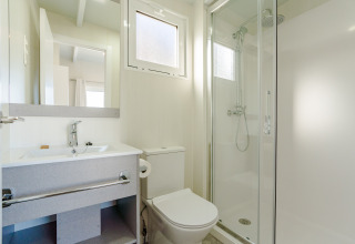 Moderne og lys badeværelse på en lodge med brusekabine, toilet, håndvask og stort spejl.