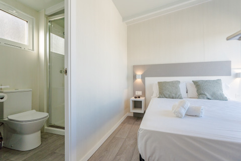 Habitación luminosa en una cabaña con cama doble, dos almohadas, toallas limpias y baño privado con ducha.