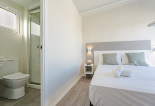 Habitación luminosa en una cabaña con cama doble, dos almohadas, toallas limpias y baño privado con ducha.