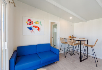 Soggiorno luminoso in lodge con divano blu, quadro di pesci colorati e tavolo da pranzo con sedie intrecciate.