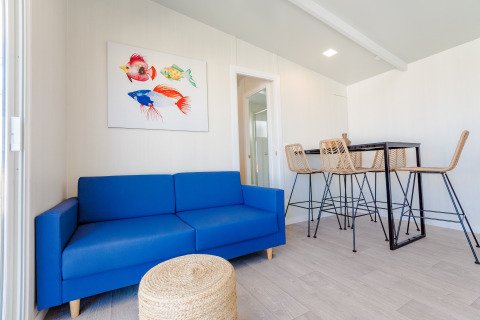 Sala de bungalow moderna con sofá azul, puf de mimbre y mesa alta en Camping Costa del Sol Glamping Village.