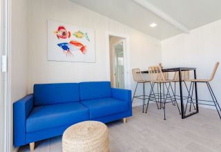 Sala de bungalow moderna con sofá azul, puf de mimbre y mesa alta en Camping Costa del Sol Glamping Village.