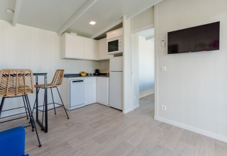 Interior de lodge moderno con cocina compacta, sillas altas, televisor de pared y suelos de madera clara.