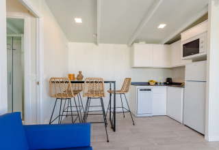 Cocina moderna en lodge con cuatro taburetes de mimbre, mesa alta, muebles blancos y sofá azul al frente.