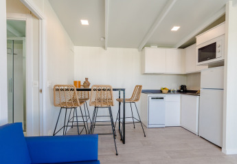 Modern lodge kitchenette with four wicker barstools, high table, white cabinets, and a blue sofa foreground.