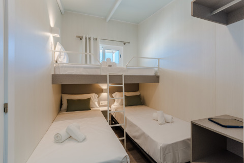 Habitación de lodge moderna y compacta con dos camas individuales, una litera y escritorio pequeño.