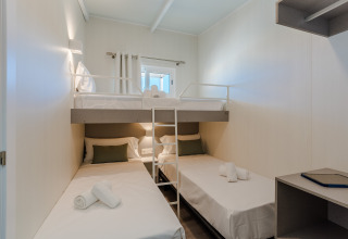 Habitación de lodge moderna y compacta con dos camas individuales, una litera y escritorio pequeño.