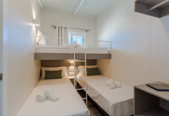 Chambre de lodge moderne et compacte avec deux lits simples, un lit superposé et un petit bureau.