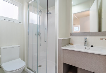 Moderne badeværelse på et lodge med brusekabine, toilet og stor håndvask under spejl og naturligt lys.