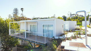 Bungalow Leo Sea View, moderno bungalow bianco con balcone e terrazza, immerso nel verde sotto il sole.