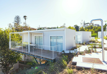 Bungalow Leo Sea View, moderno bungalow bianco con balcone e terrazza, immerso nel verde sotto il sole.