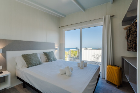 Soveværelse med dobbeltseng, havudsigt, moderne indretning og gul kuffert på Bungalow Leo Sea View.