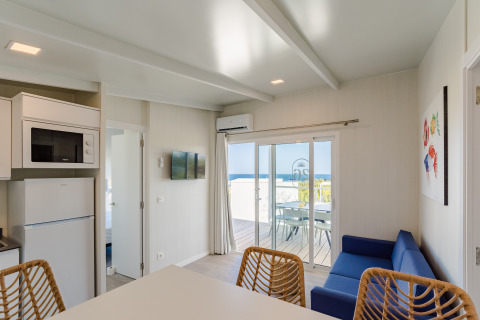 Interior de bungalow moderno con vistas al mar, sofá azul y terraza en Camping Costa del Sol Glamping Village.