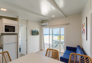 Interior de bungalow moderno con vistas al mar, sofá azul y terraza en Camping Costa del Sol Glamping Village.